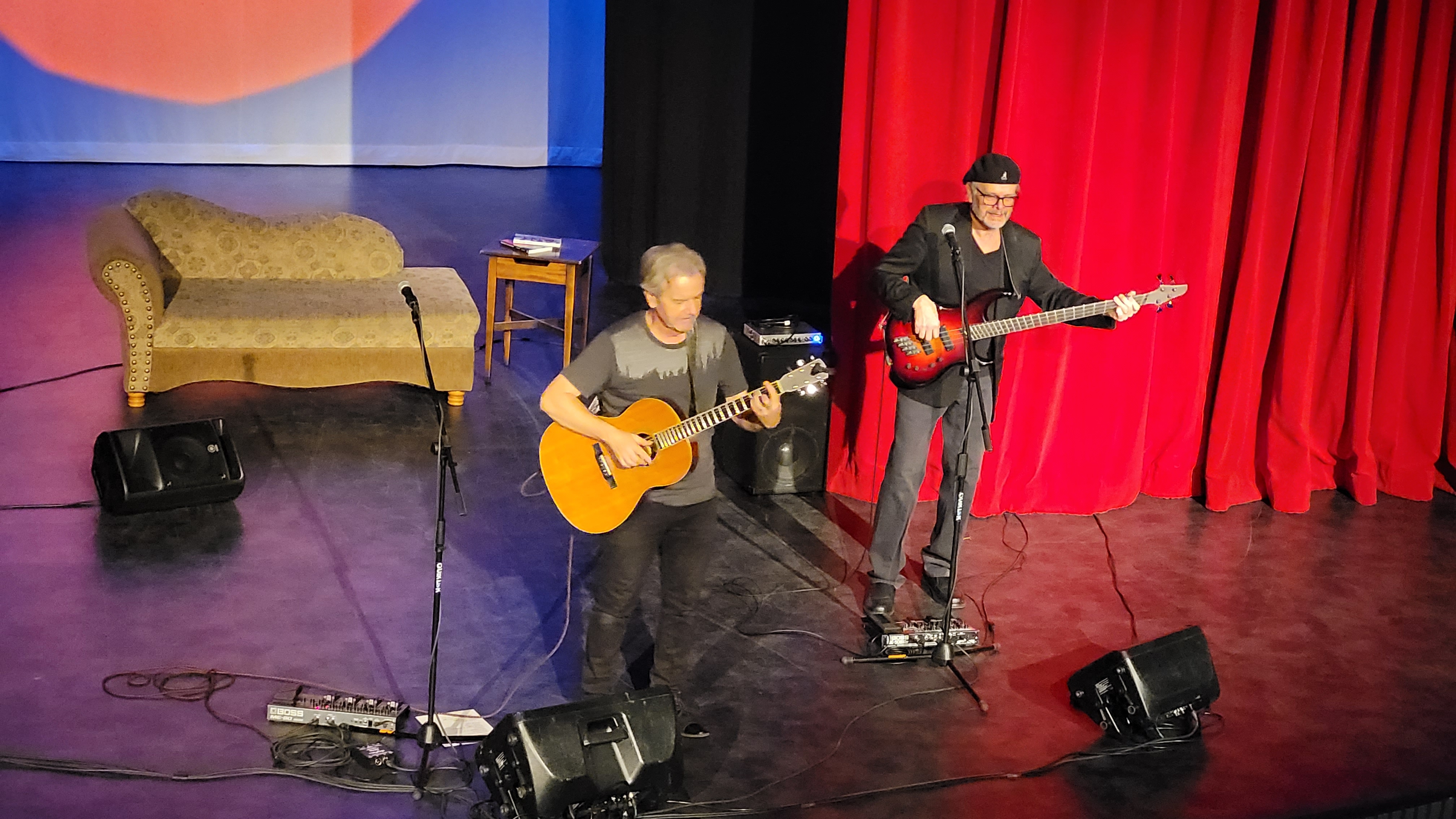 Jack Semple performing an acoustic set with a bass player on a theater stage with red drapery